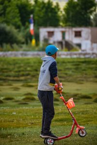A young boy riding a red kids kick scooter through a lush green field