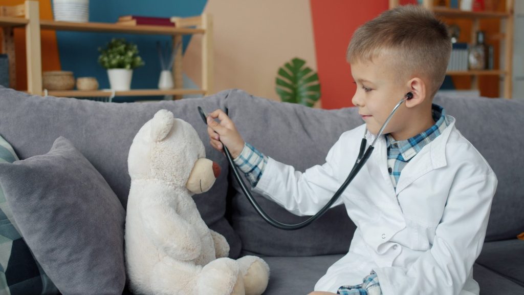 Boy in doctor's coat listens to teddy bear